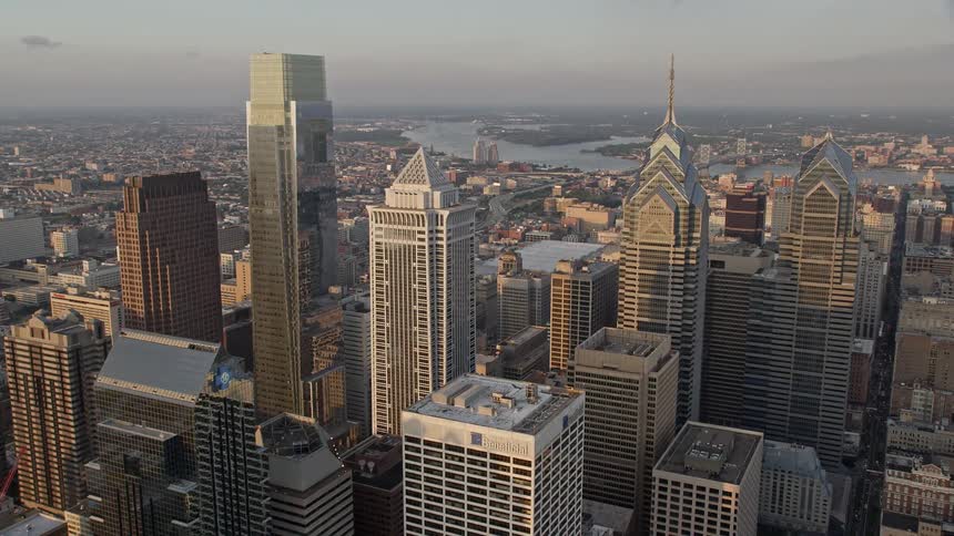 An aerial view of Philadelphias downtown area at dusk approaching the towering skyscrapers to reveal the convention and exhibition centers Philadelphia City Hall and other iconic structures amidst partly cloudy skies during the evening