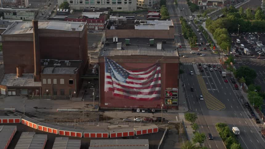 Aerial footage of a large American flag mural on a warehouse building in Philadelphia during sunset