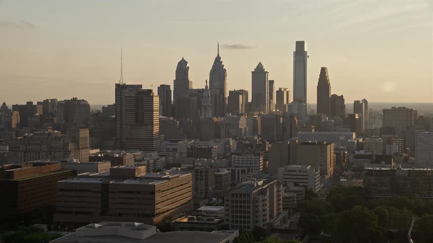 Approaching Downtown Philadelphia skyline during sunset captured from an aerial with high rises and skyscrapers towering over the hazy metropolis