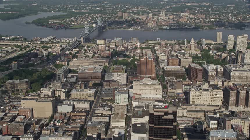 Aerial view of downtown Philadelphia including office buildings and the Benjamin Franklin Bridge approaching the bridge while flying over the citys rivers and waterways on a partly cloudy day