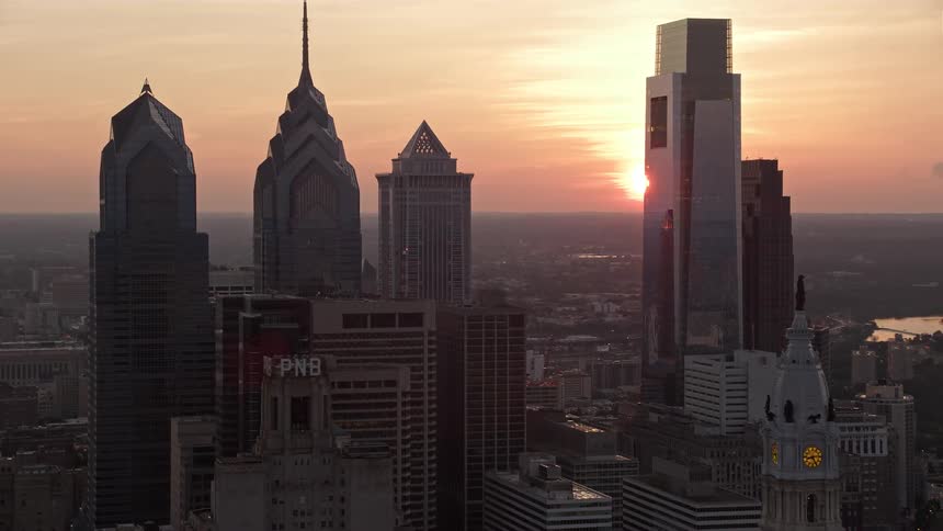 Aerial footage of Philadelphias downtown featuring towering skyscrapers and City Hall with a stunning sunset as the backdrop
