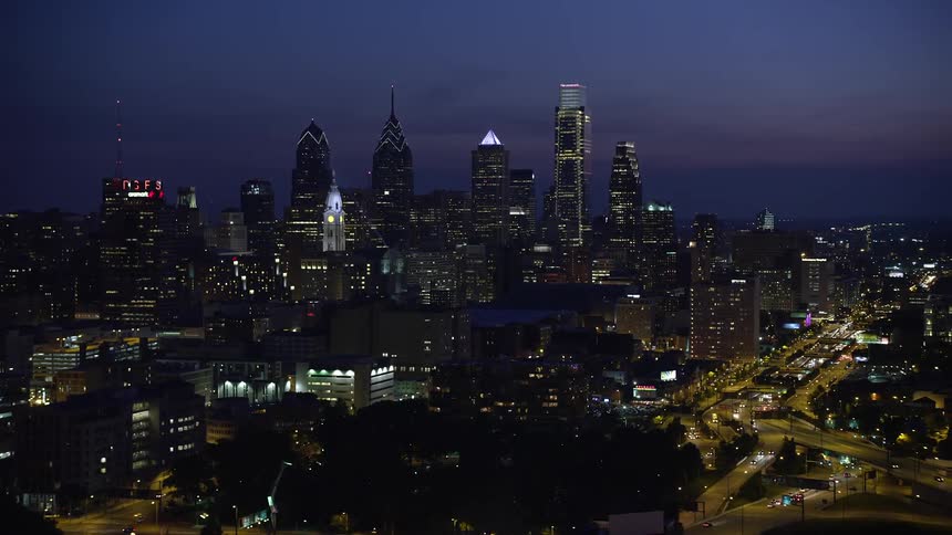 A stunning aerial view at night captures Downtown Philadelphias skyline showcasing towering skyscrapers and high rises against a partly cloudy sky over the metropolitan area