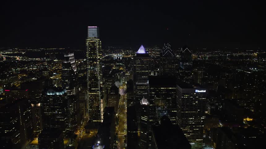 Aerial footage captures illuminated skyscrapers and high rises as traffic moves through Philadelphias metropolitan skyline at night culminating in a view of the historic Philadelphia City Hall