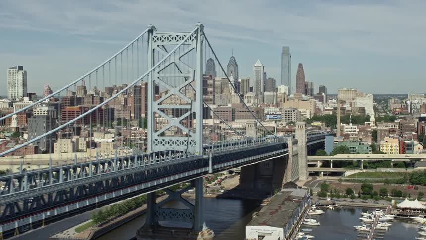 A stunning aerial view of the Benjamin Franklin Bridge panning to reveal the beautiful Downtown Philadelphia skyline during daytime