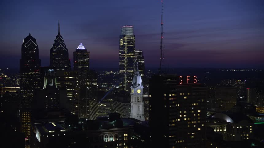Downtown Philadelphias towering skyscrapers and striking City Hall clock tower illuminate the night skyline in this aerial stock footage of Pennsylvanias historic landmarks