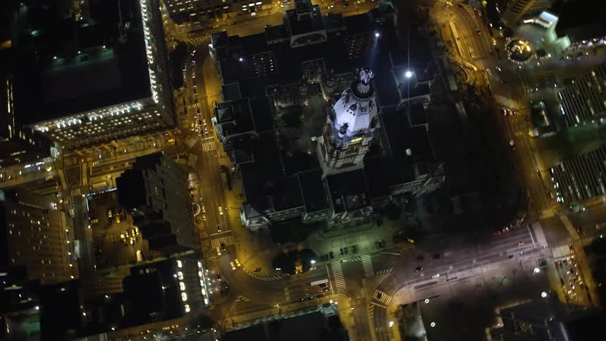 A breathtaking aerial footage captures the iconic Philadelphia City Hall in the heart of downtown bathed in bright lights revealing the famous William Penn statue on top and providing a mesmerizing birds-eye view of the bustling metropolis below on a clea