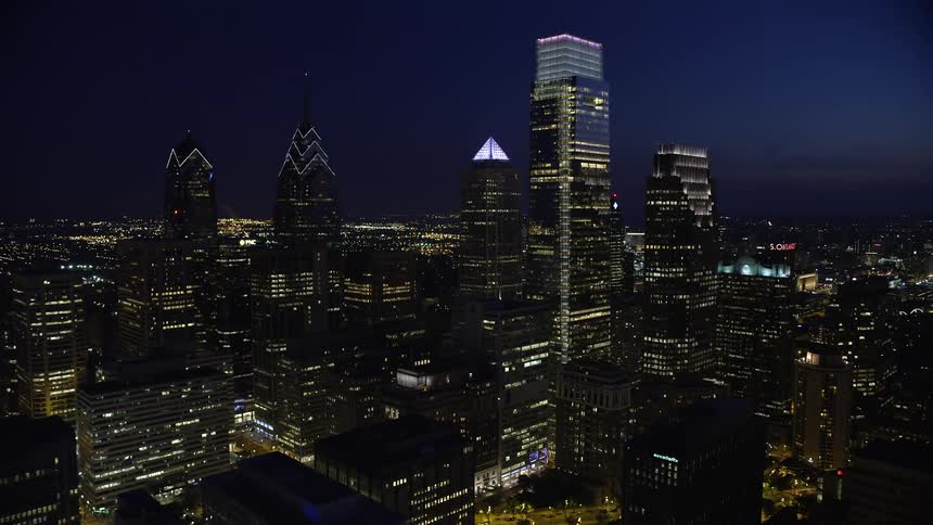 Flying over Downtown Philadelphias tallest skyscrapers and City Hall at night in Pennsylvania during partly cloudy skies
