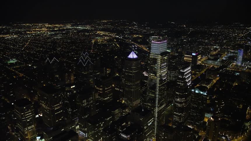 Aerial footage of Philadelphias downtown skyline at night flying by the historic City Hall and other iconic skyscrapers such as One and Two Liberty Place and the Comcast Center