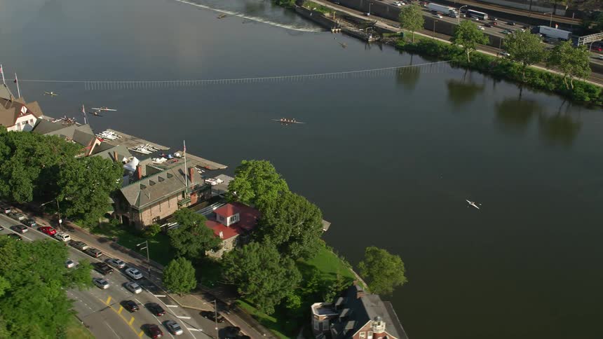 Aerial footage of rowers passing by Boathouse Row on the Schuylkill River in Philadelphia during a partly cloudy day