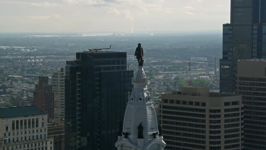 Approaching the iconic William Penn statue on top of Philadelphia City Hall during a hazy daytime in an aerial shot