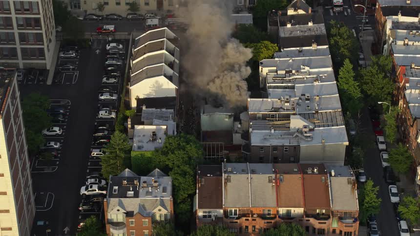 Aerial footage follows a residential fire near Downtown Philadelphia as dark smoke rises from a burning building and a fire truck is on the scene during sunset