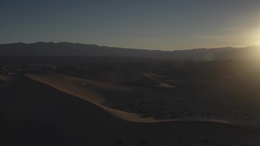 Sand dunes in a desert are bathed in sunlight