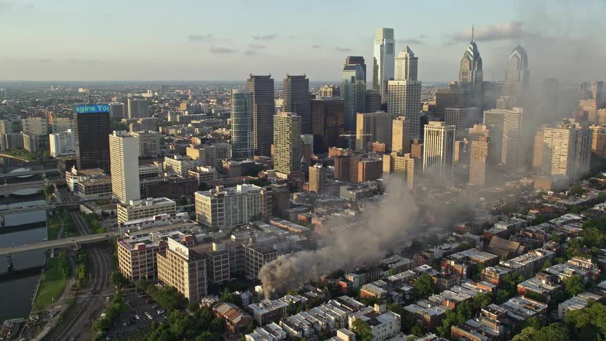 Aerial footage at sunset captures a residential fire in downtown Philadelphia as smoke rises into the hazy skyline near the river