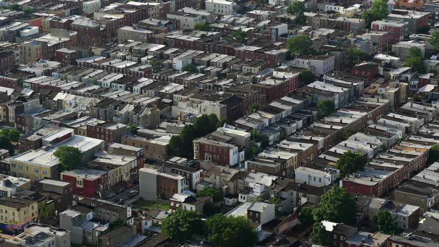 Aerial footage of busy city streets and residential row houses in the South Philadelphia neighborhood with partly cloudy skies during the spring or summer season