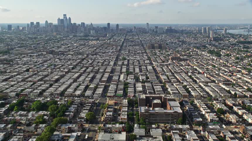 Aerial footage flying over the bustling neighborhoods of South Philadelphia offering a stunning side view of the downtown skyline in sunny weather
