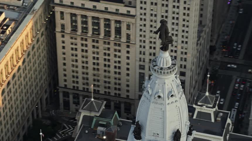 Aerial footage at sunset captures the iconic William Penn statue atop Philadelphia City Hall a historic landmark in the bustling downtown area