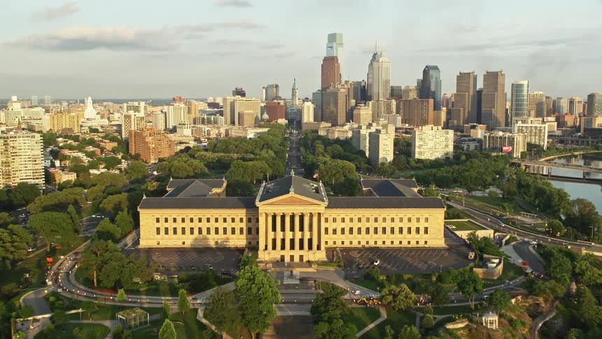 A stunning aerial view of Philadelphia at sunset panning across the Schuylkill River to reveal landmarks like Boathouse Row Museum of Art City Hall and skyscrapers with clear skies and clear waters below