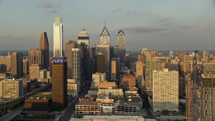 A breathtaking aerial footage of downtown Philadelphia skyscrapers at sunset with partly cloudy skies and magnificent architecture