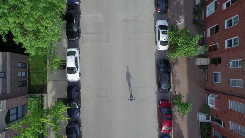 A skateboarder is seen from above as he winds his way down an empty residential street