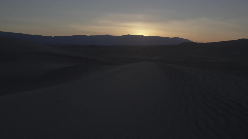 The sun sets over sand dunes and mountains