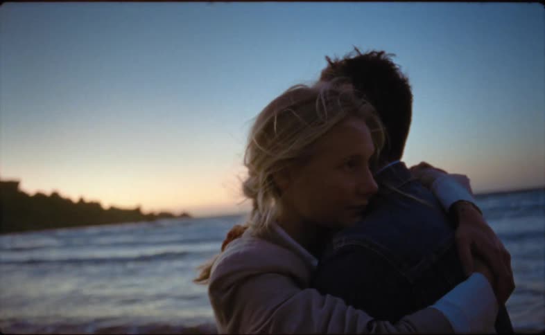 A man and woman stand on a beach and hug one another