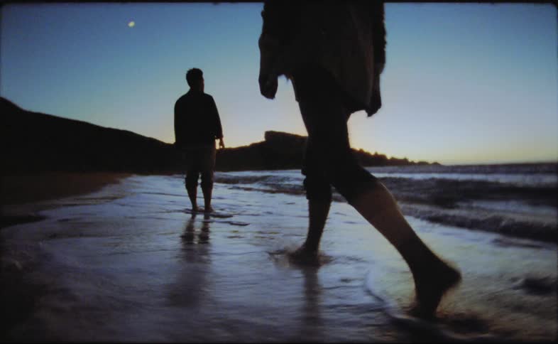 A man and woman wade along the beach at night