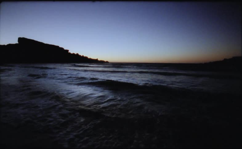 Landscape of ocean waves breaking against the shore at dusk