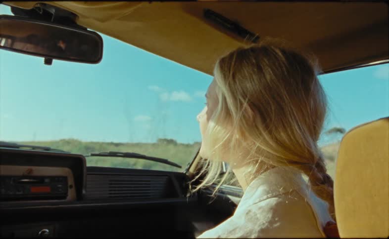 A blonde woman sitting in the passenger seat of a vehicle while travelling through the countryside