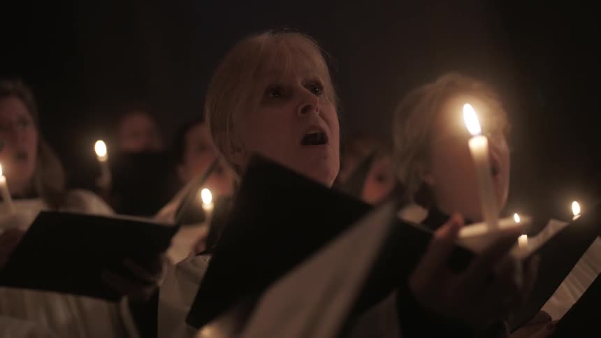 Women singing in a church choir during a candlelight service