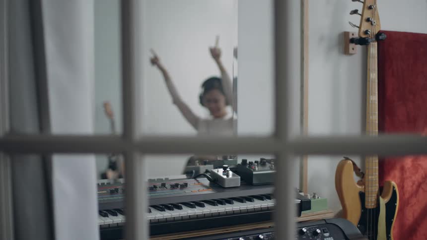 Woman wearing headphones spins in wheeled chair before approaching keyboard to play it