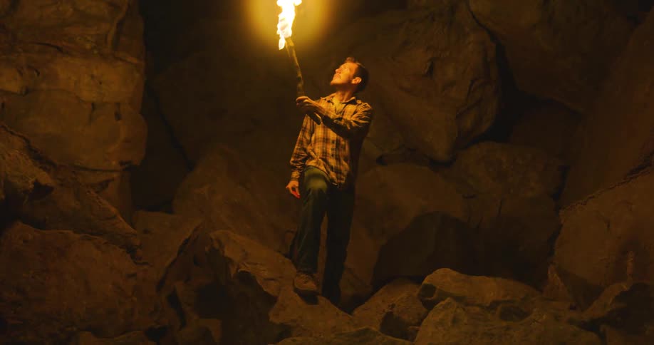 A man using a torch to look at rocks in a mountain