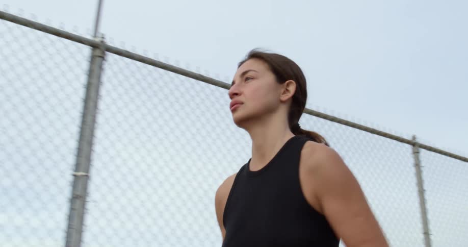 Woman jogs by chain link fence overlooking town in valley