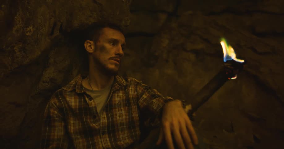 Man leans against natural rock wall holding a burning torch