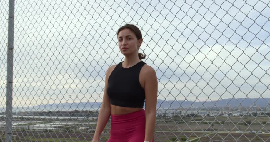 The view is of a woman that is standing against a fence in the day time