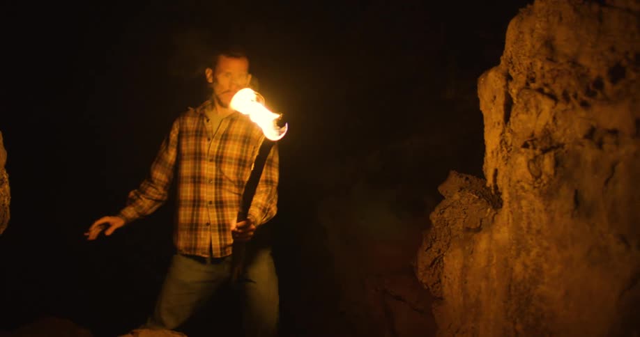 A man is carrying a torch as he walks through a dark cave
