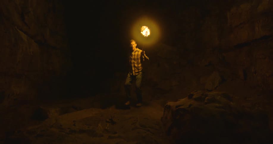 A man is carrying a torch as he walks through a dark cave