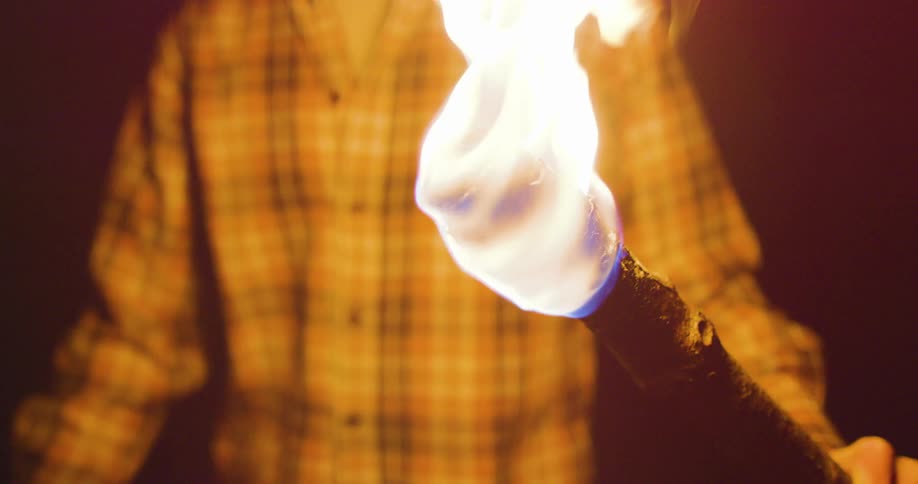 A man is lighting up a torch with fire inside of a cave
