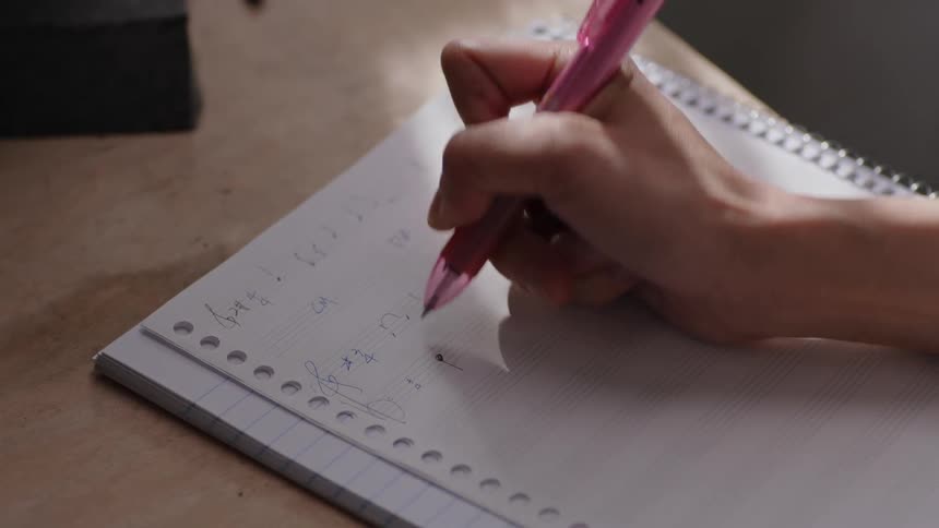 A persons hand is holding a pen as they write in a spiral notebook on a table