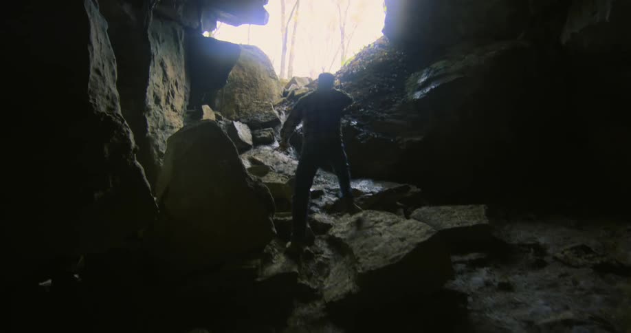 Man climbs along boulders leading to mouth of dim cave