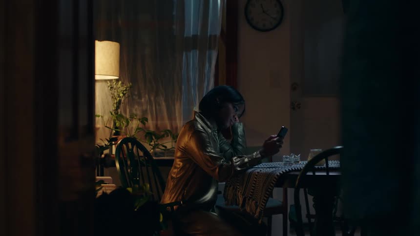 A woman scrolls through her phone while sitting at her dining room table