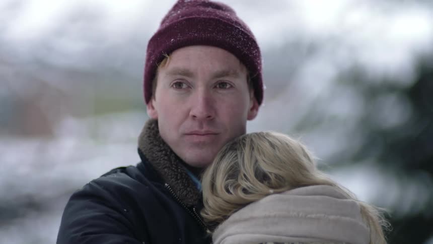 Man holds woman close as they hug while standing outdoors on snowy day