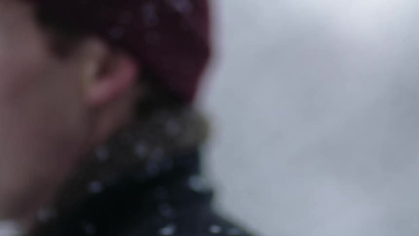 A man is standing outside with snow on his coat collar as it snows on a winter day