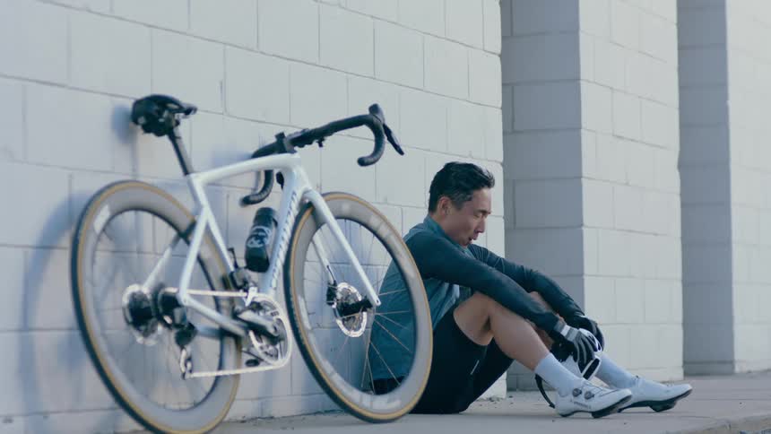 A man is sitting on sidewalk while breathing heavily next to his bicycle in the daytime