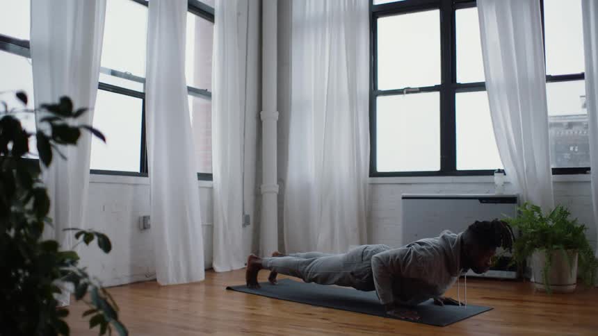 A man doing yoga at home moves into a downward dog position