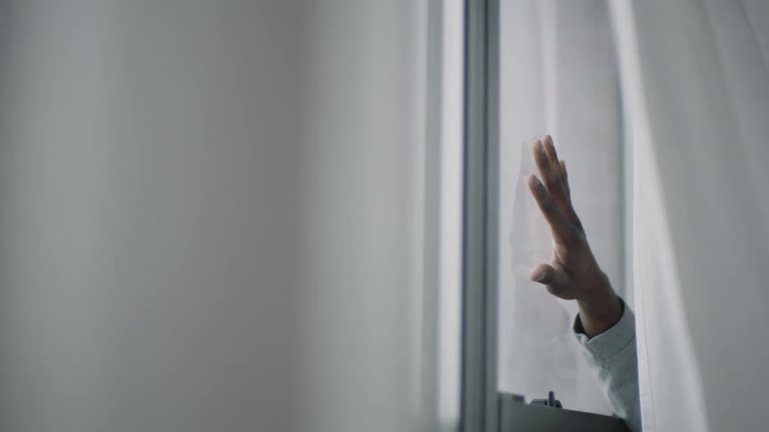 Curtain blows back to show persons hand on window glass