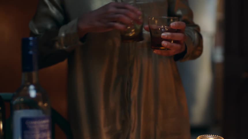 A woman walking to a table picking up three glasses and walking into the kitchen