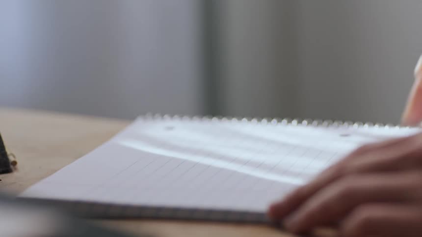 A female holds a pen as she prepares to write in a spiral bound notebook