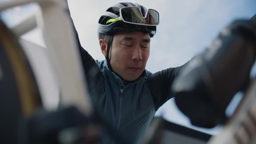 A man wearing a cycling helmet is bending down looking at his bicycle and he stands up