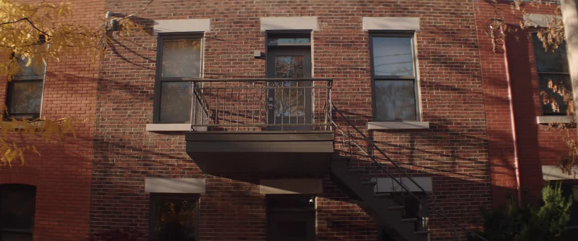 A set of stairs leads to a landing outside of an apartment building with a brick facade