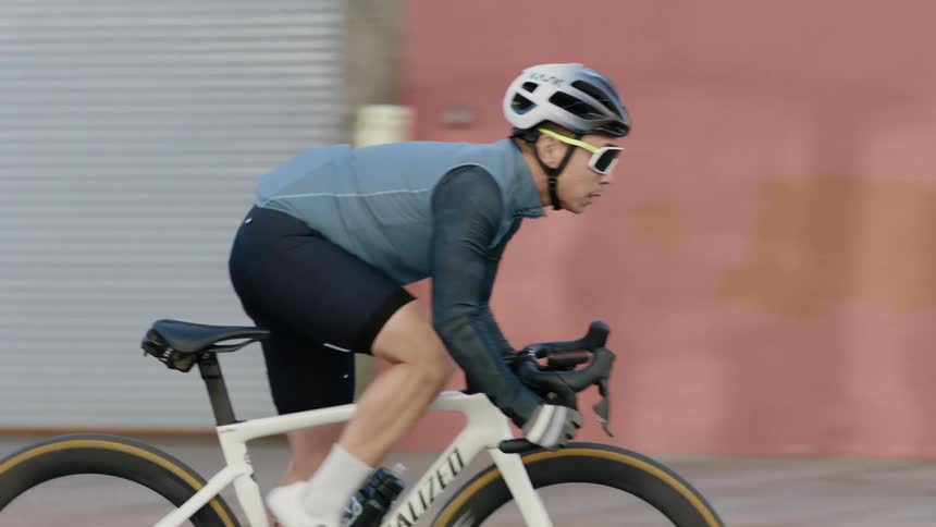 Cyclist with helmet sunglasses cycling jersey big shorts and cycling shoes pedals down the street passing by trucks